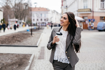 Obraz premium Beautiful business woman drinks coffee on a street