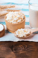 Cottage cheese, glass of milk, two eggs, wooden spoon with cottage cheese and wheat ears lie on the napkin from a burlap on the old wooden table