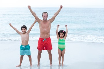 Father and children standing with arms raised at beach