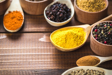 Beautiful colorful spices in wooden spoons and bowls on an old wooden brown table. Free space for your text
