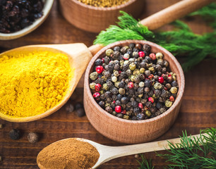 Beautiful colorful spices in wooden spoons and bowls on an old wooden brown table with green dill
