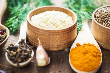 Beautiful colorful spices in wooden spoons and bowls on an old wooden brown table with green dill