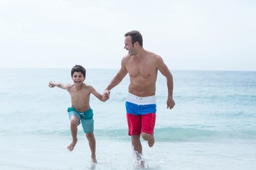 Father and son holding hands while running at beach 