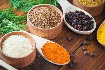 Beautiful colorful spices in wooden spoons and bowls on an old wooden brown table with green dill