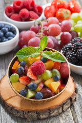 fruit salad in a bamboo bowl and fresh berries, vertical