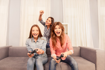 Three happy attractive girls sitting on sofa and playing video g