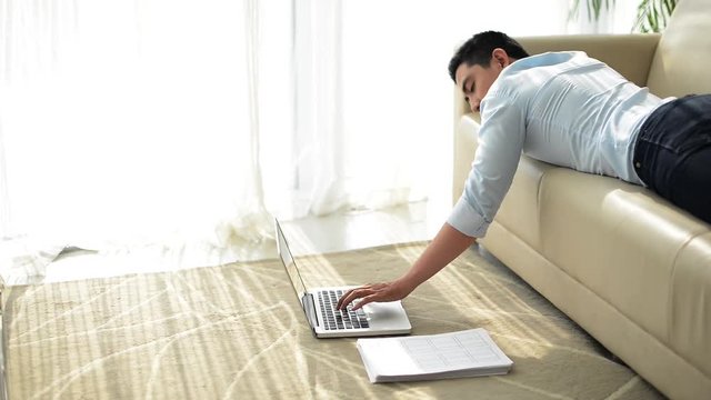 Cinemagraph of Vietnamese young businessman man typing on laptop when lying on the sofa