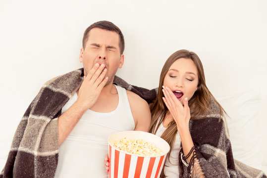 Couple in love sitting with popcorn and yawning while watching f