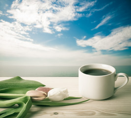 Tea cup with tulips on the wooden table opposite blurred backgro