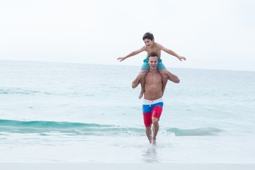 Happy father carrying son while running at beach 