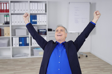 mann im büro streckt lachend die arme nach oben und ballt die fäuste