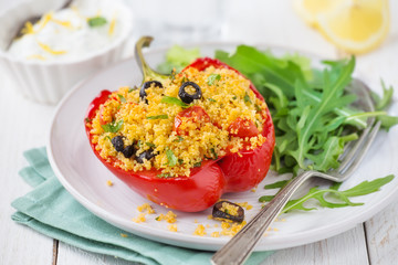 Vegetarian couscous stuffed pepper with rocket salad and yoghurt condiment on white wood background