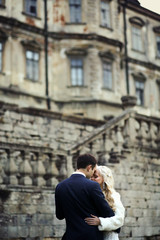 Fototapeta na wymiar blonde bride and brunette groom walking near old castle