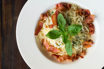 top view of spaghetti white sauce with bacon in white ceramic dish. object on dark wood table deck
