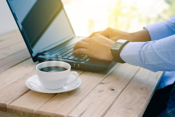 Coffee cup with closeup man typing a laptop on wooden table.