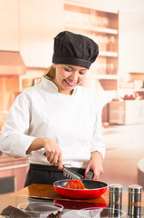 Woman chef wearing full cooking outfit standing frying vegetables in red skillet