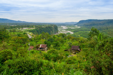 Obraz premium Fantastic overview of amazon jungle valley with river and waterfalls in the distance, some simple small houses located sorrounded by forest