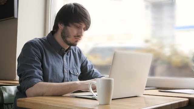 Happy Young Man Freelancer with Modern Laptop in Cafe taking Cup of Coffee