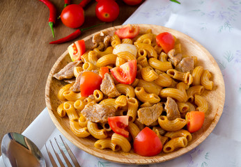 Fried macaroni with pork and vegetable in tomato sauce in plate placed on a wooden table