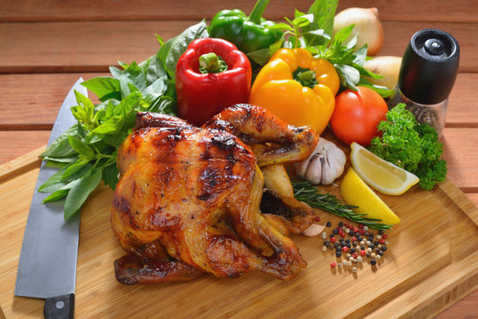 Roast chicken and various vegetables on a chopping wood
