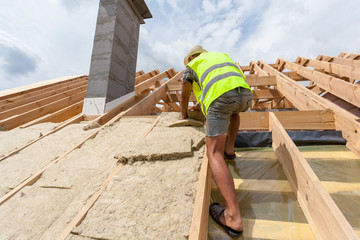 Roofer builder worker installing roof insulation material on new house under construction
