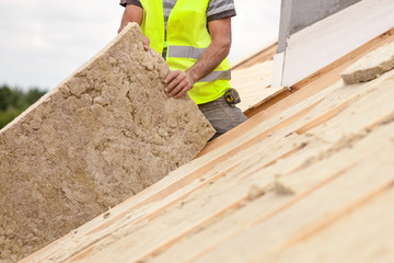 Roofer builder worker installing roof insulation material on new house under construction