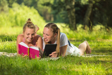 Fototapeta premium Girl in the meadow reading a book and a tablet