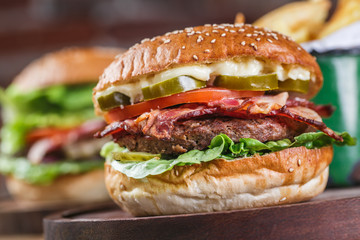 Close up on fresh burger in bun with sesame with lettuce, tomato, beef and bacon.