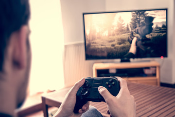 Playing game on console - hands holding game pad and playing shooter game on tv screen.