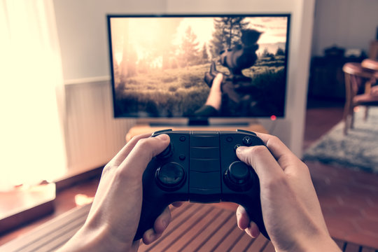 Playing game on console - hands holding game pad and playing shooter game on tv screen.