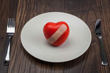 red heart on a plate, fork and knife on a wood background