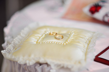 golden wedding rings on white ring bearer pillow