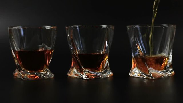 Whiskey being poured into a glass against black background. Long shot. 