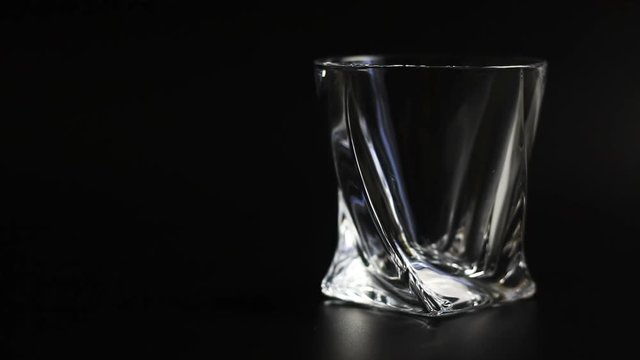 Whiskey being poured into a glass against black background. Close up. 