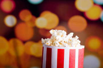 Closeup red white striped container standing up with popcorn reaching over edge, low angle, flashy...