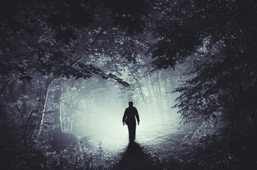 surreal light in dark forest and man silhouette