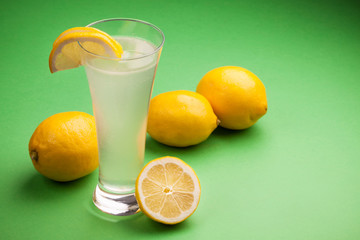 Glass of water and fresh lemon on a green background