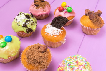 Multiple muffins decorated with mulicolored frosting, cocoa powder and beans, candies and whipped cream top view toned selective focus