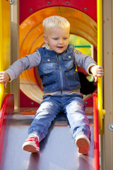 Blonde little boy sits on a childrens slide at the playground