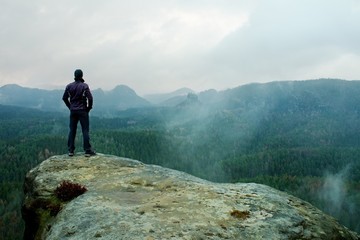 Hiker on sharp cliff of sandstone rock in rock empires park and watching over misty and foggy spring valley