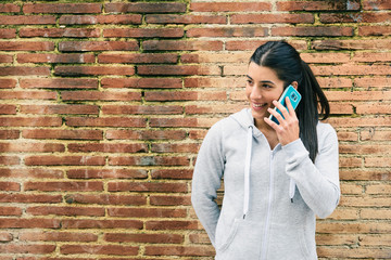 Natural sporty woman calling on smartphone in the street against a brick wall. Urban fitness athlete on cellphone call during workout rest.