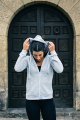 Sporty fitness woman getting ready for urban workout or running. Female runner putting on the sweatshirt hood.