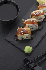 Eel sushi roll on a plate with ginger wasabi soy sauce and chopsticks over black background