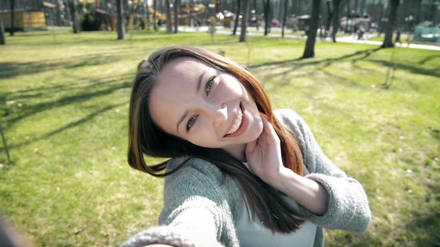 Portrait of a beautiful young woman selfie in the park with a smart phone. 