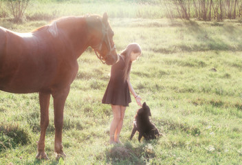 Girl leads her horse and stroking black dog