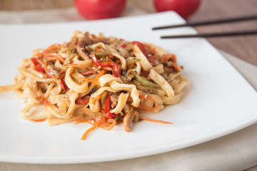 Egg udon noodles with pork, vegetables and sesame seeds on a white plate, close-up