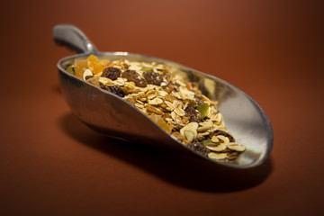 Dry muesli in a big metal spoon on the brown background