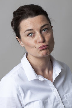 female portrait - smart mature woman with smart white shirt pouting for doubt and joy, grey background