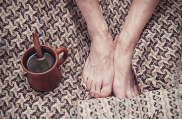 Man feet on woolen plaid and cup of coffee