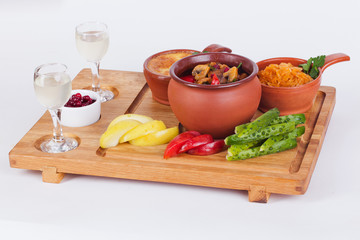 meat with mushrooms in a pot, julienne cocotte, pickles, apples, vodka wooden board isolated white background